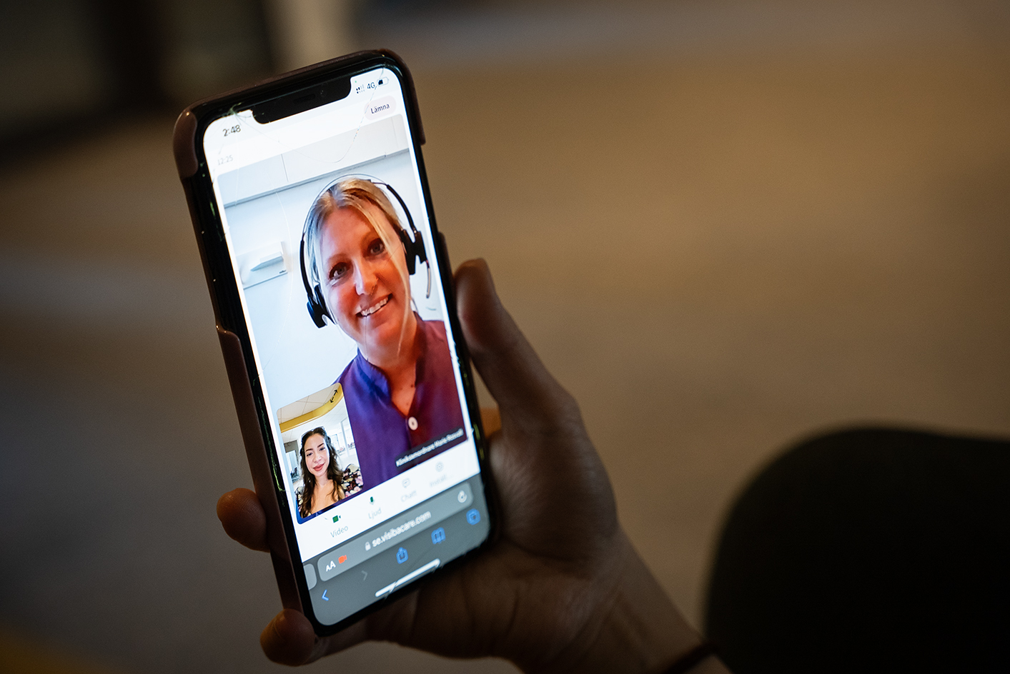 En person håller i en mobil och genomför ett digitalt besök. Kunden och behandlaren syns på skärmen.